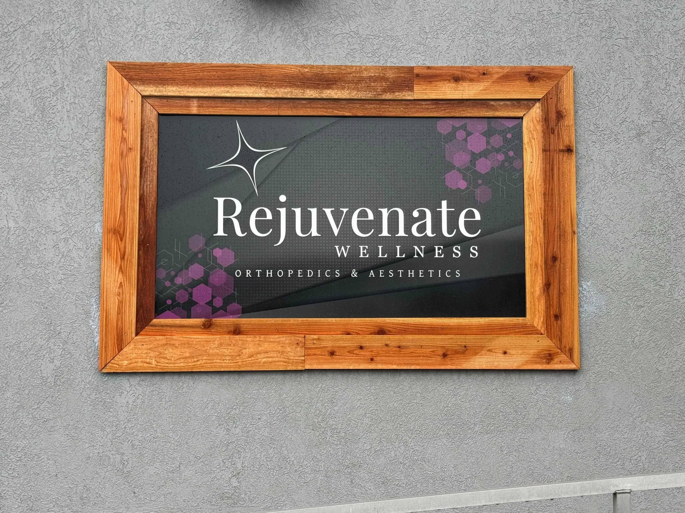 The wood-framed Rejuvenate Wellness Orthopedics & Aesthetics sign mounted on the building exterior