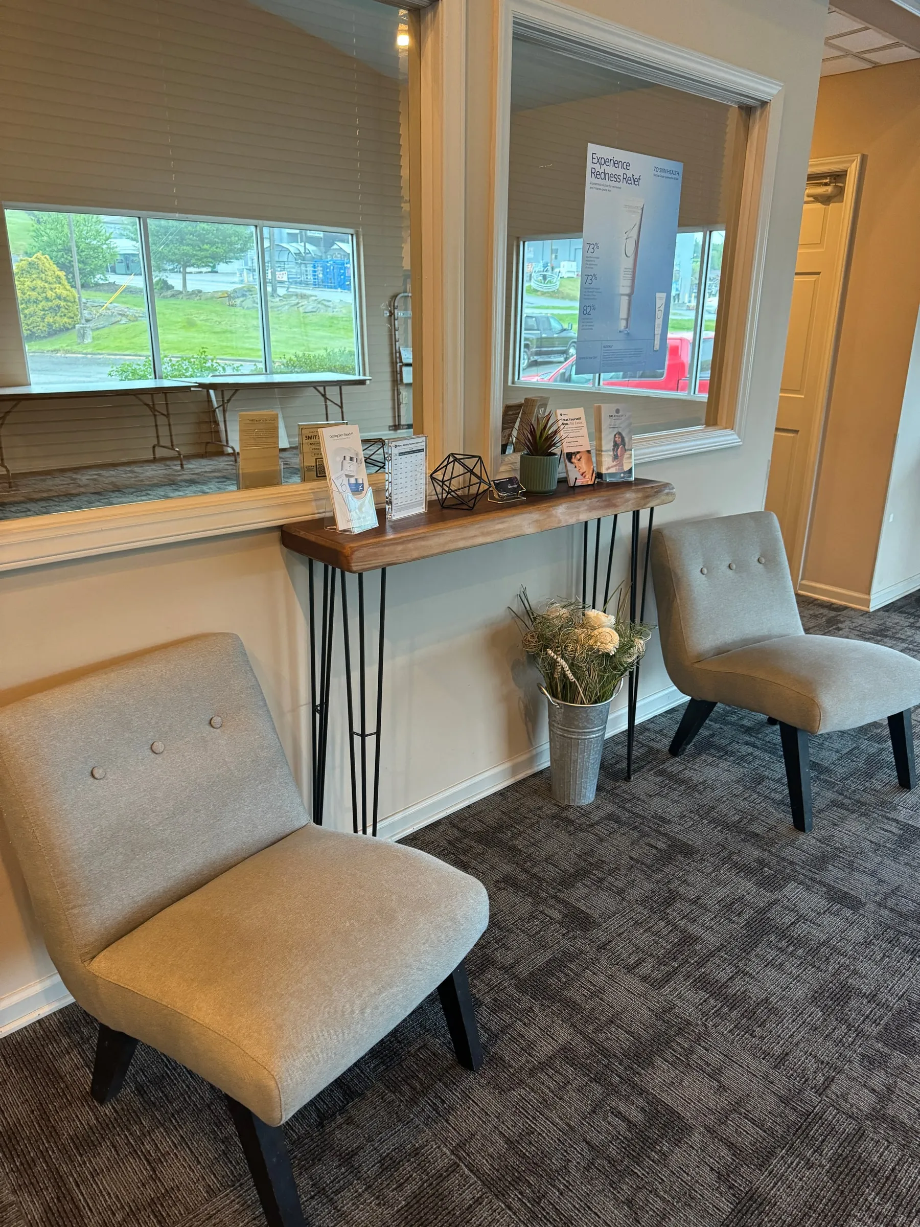Waiting area with two grey chairs and a console of fresh flowers near sunlit windows